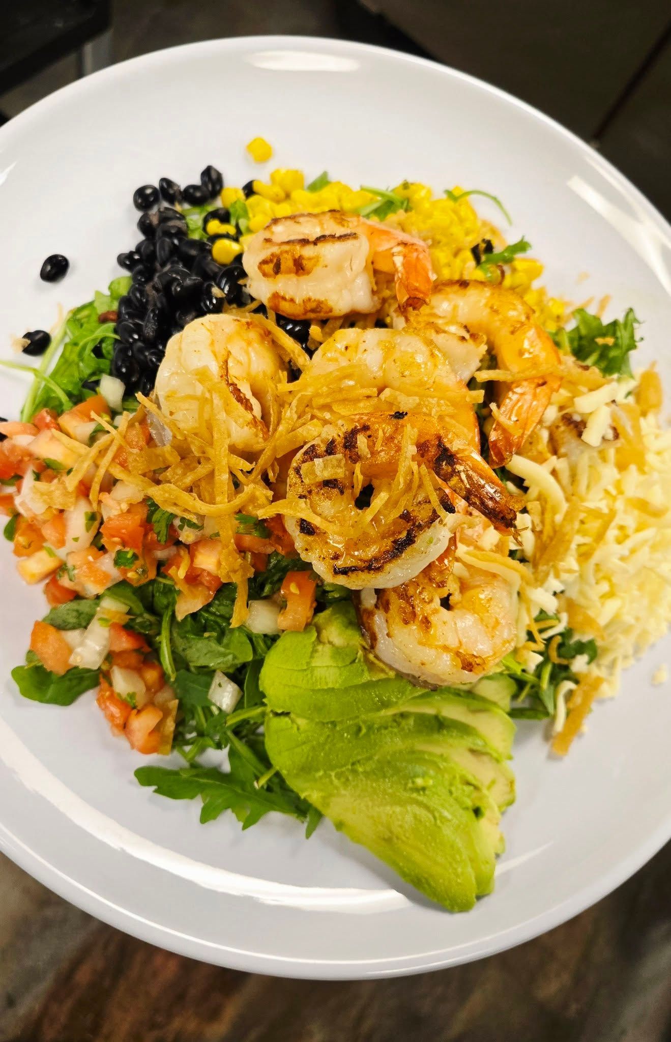 Grilled shrimp salad with avocado, corn, black beans, and pico de gallo on a white plate.