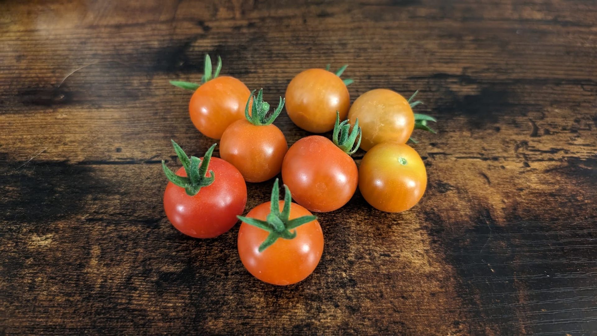 A bunch of tomatoes are sitting on a wooden table.