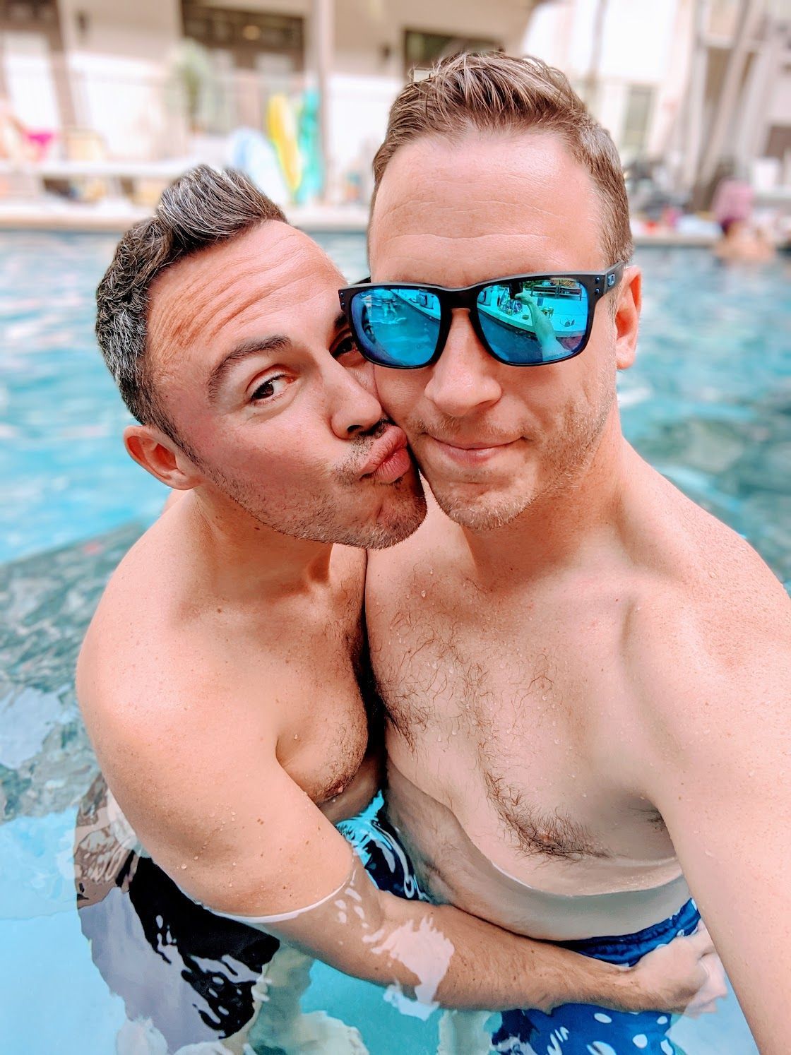 Two men are kissing in a swimming pool while wearing sunglasses.