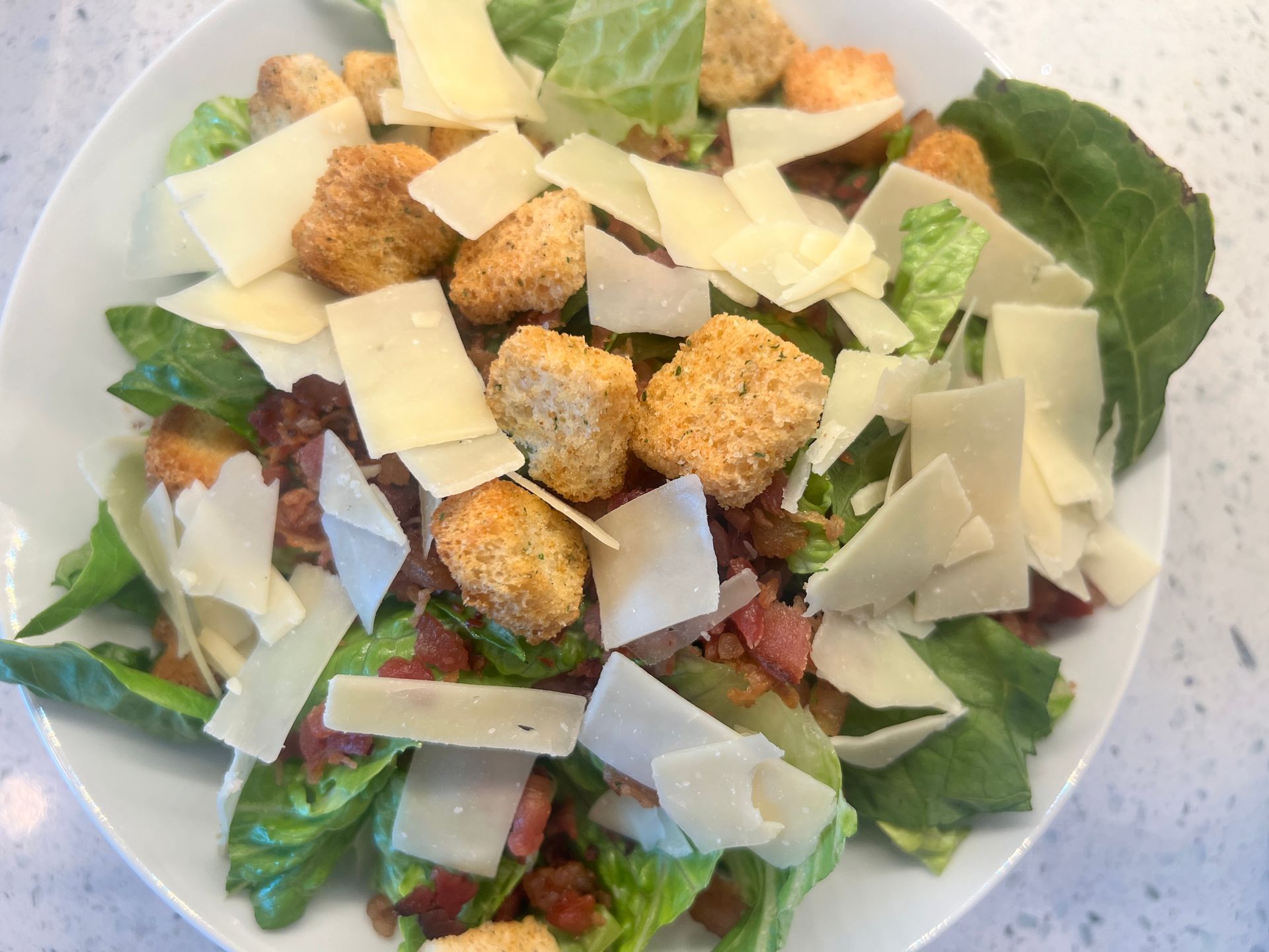 A close up of a salad with croutons and cheese on a plate.