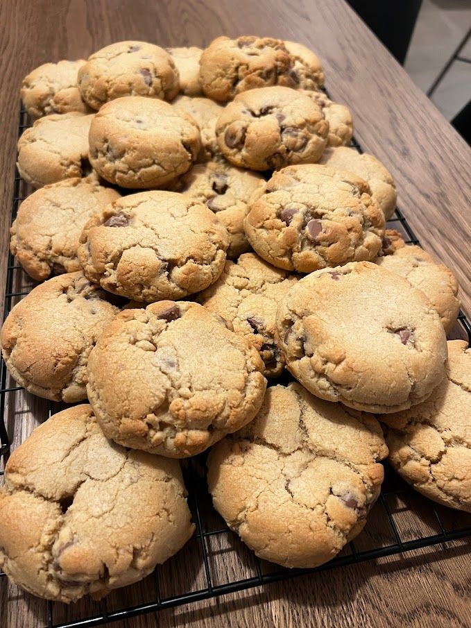 A bunch of chocolate chip cookies are sitting on a cooling rack on a table.