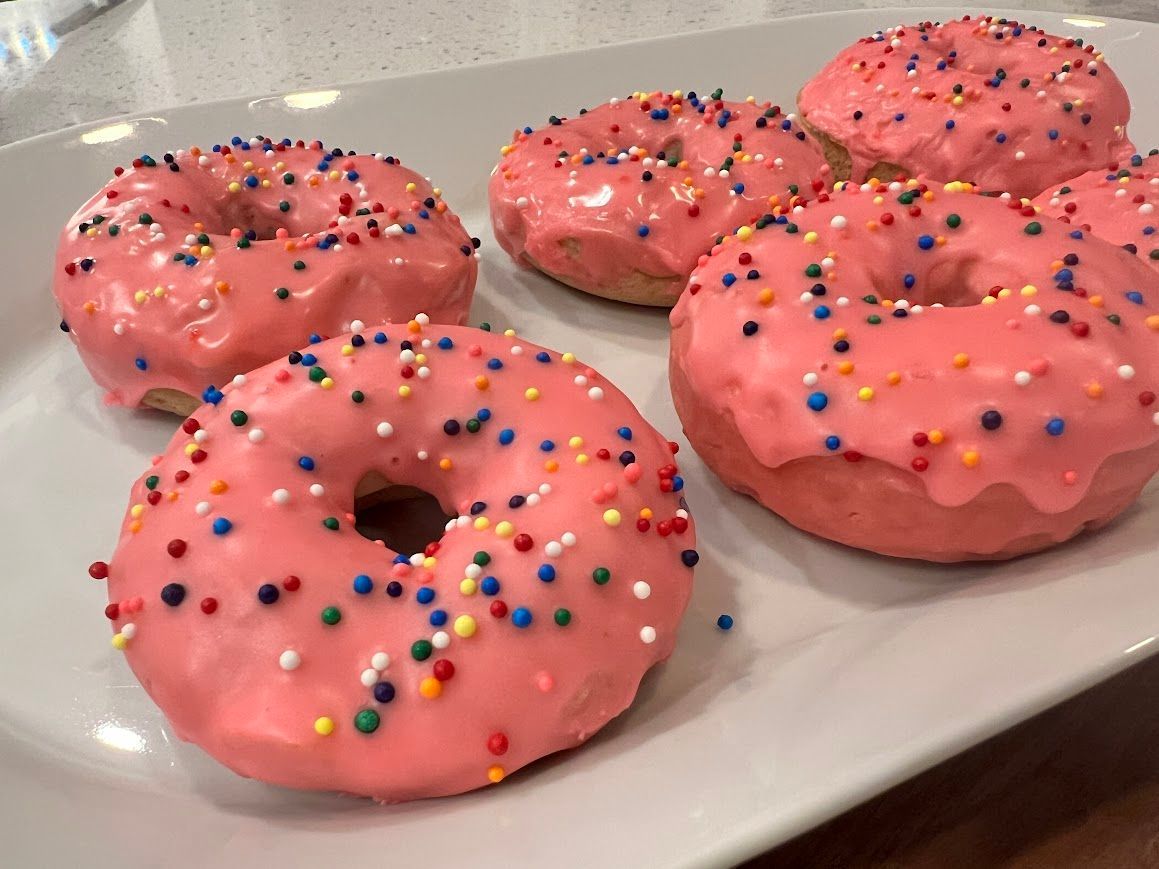Four donuts with pink frosting and sprinkles on a white plate