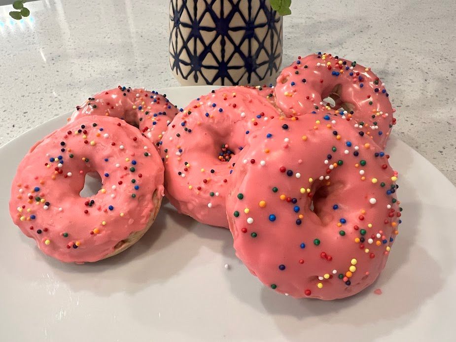 A white plate topped with pink frosted donuts and sprinkles