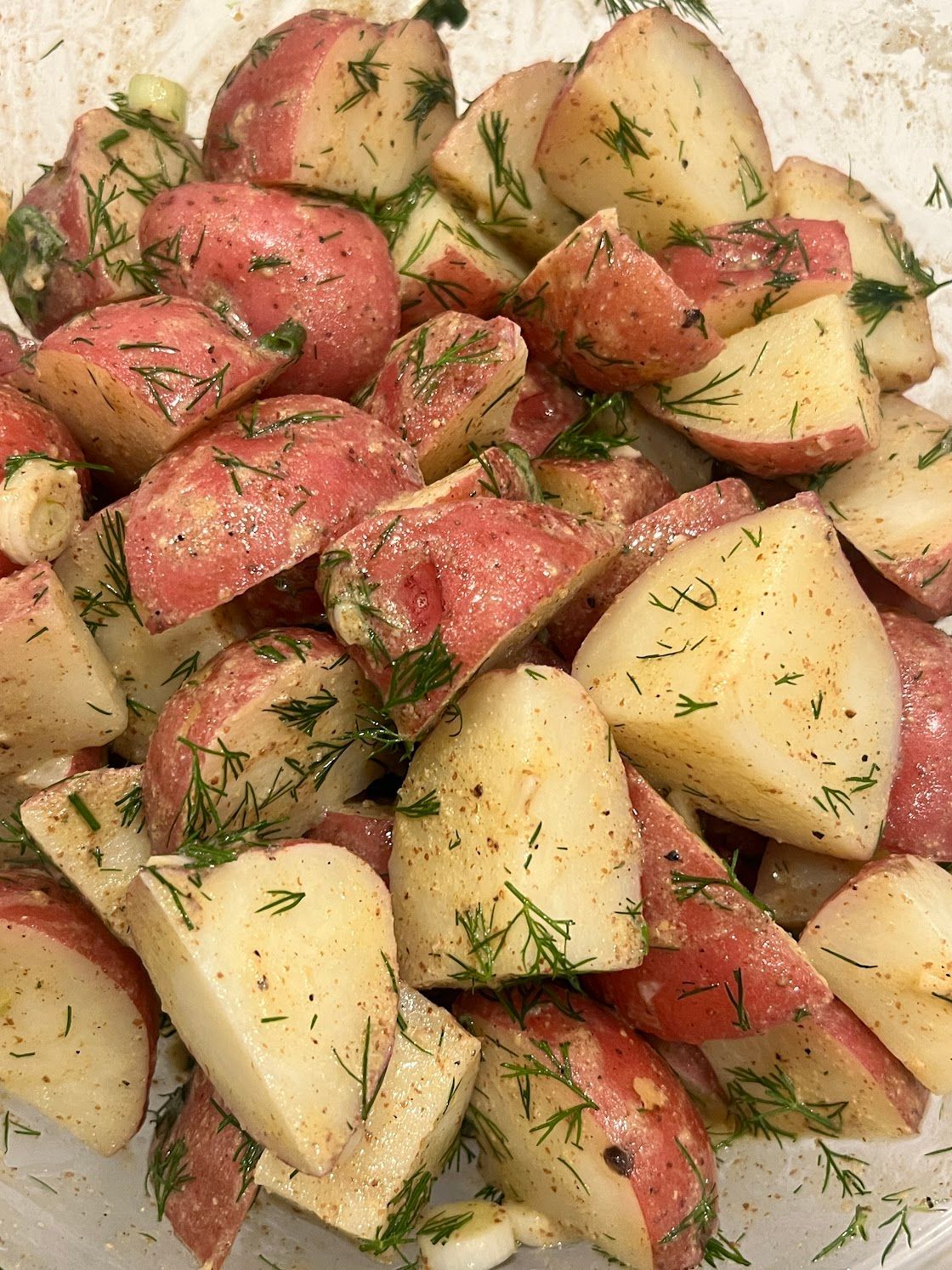 A close up of a bowl of potato salad with dill.