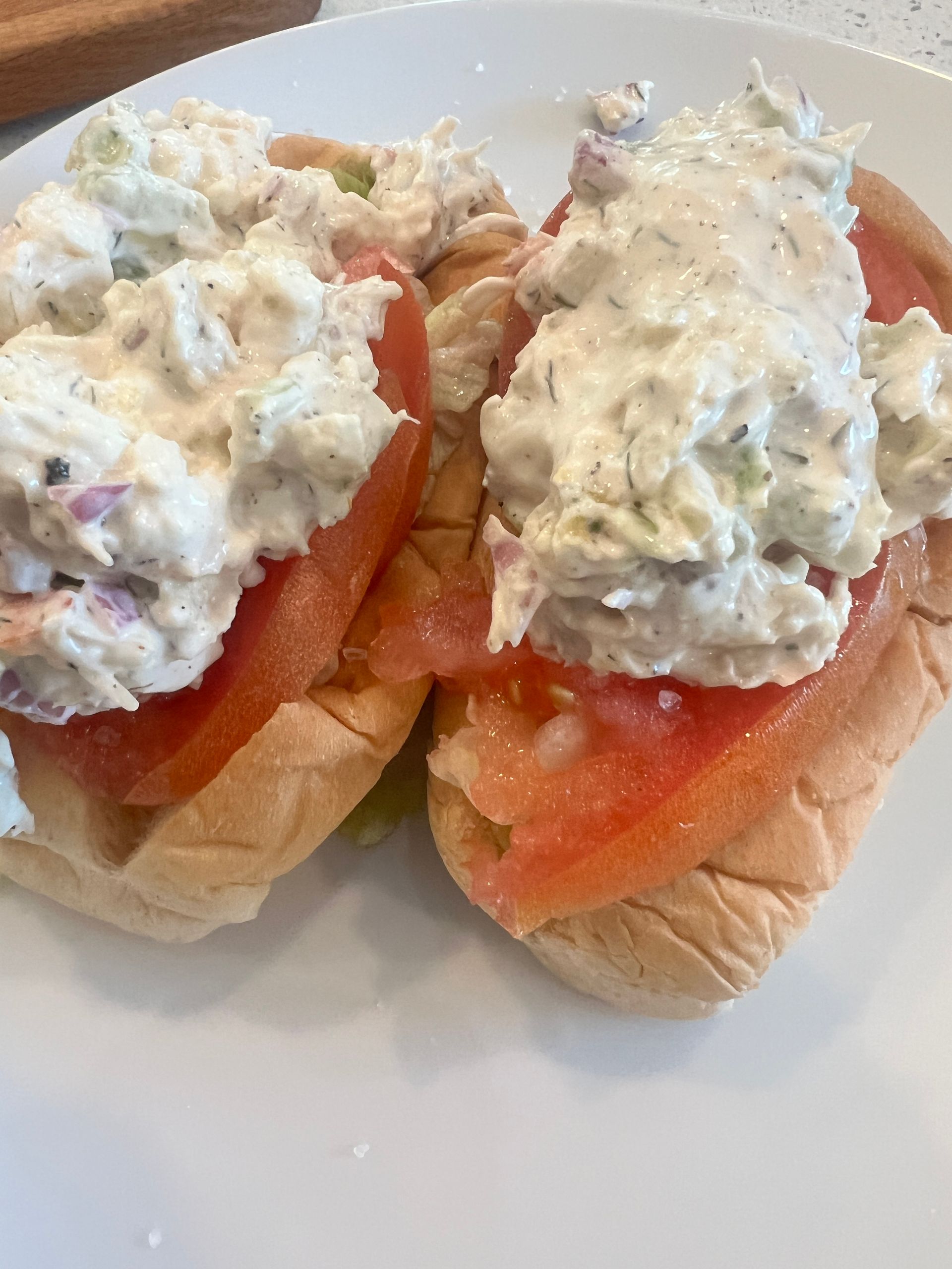 Two chicken salad sandwiches with tomatoes on a white plate.
