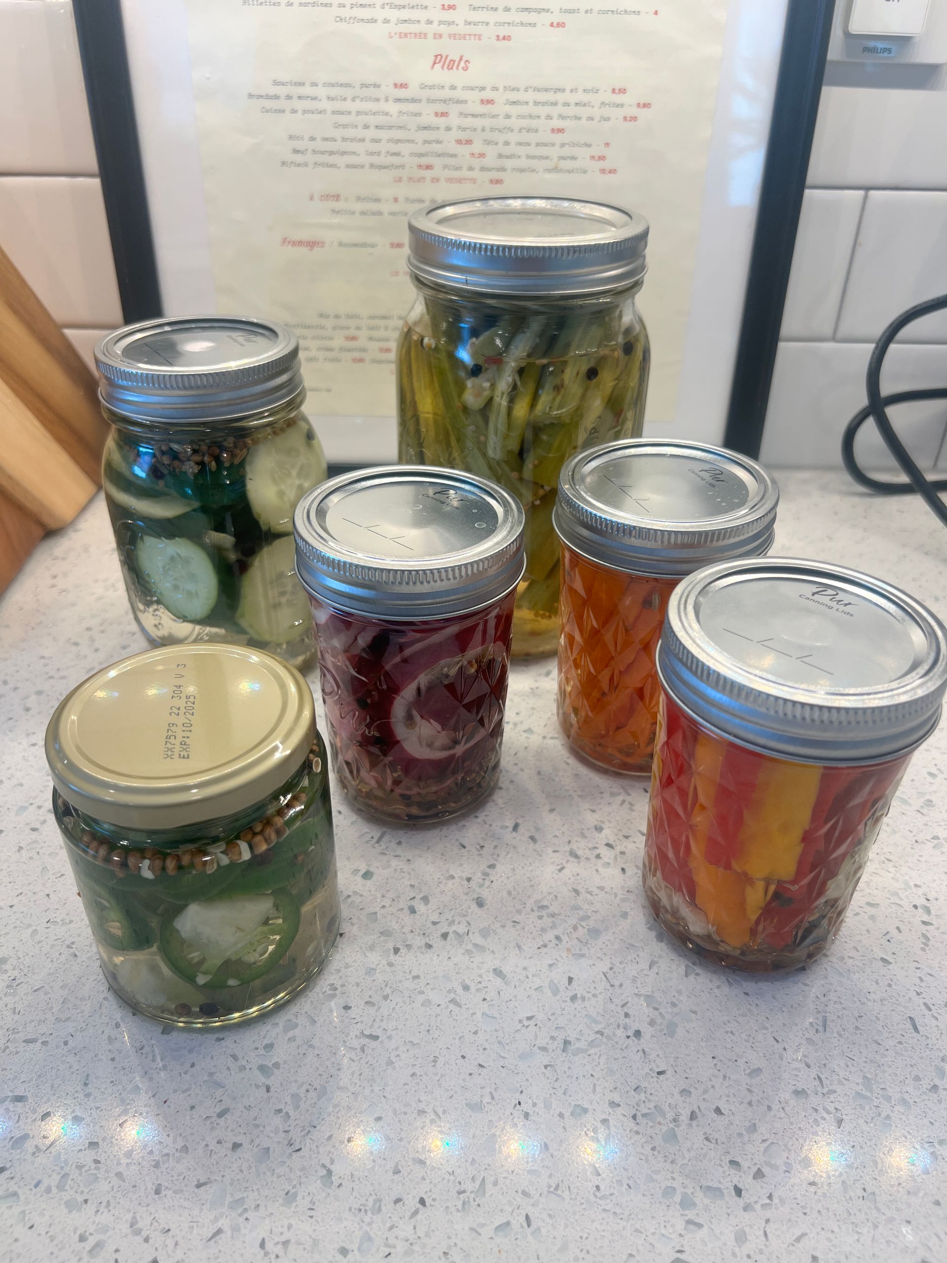 A bunch of jars of pickles are sitting on a counter.