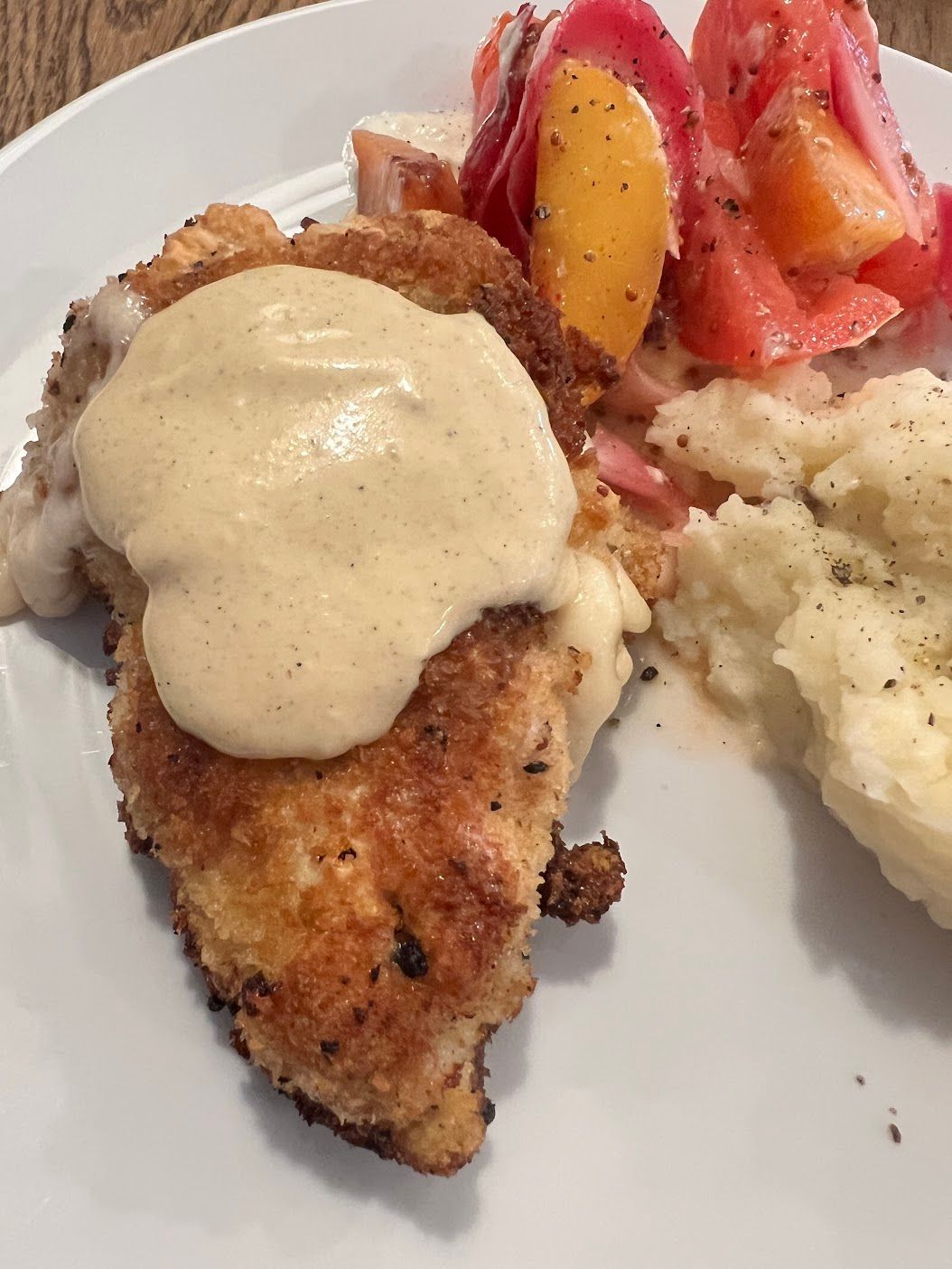 A white plate topped with chicken mashed potatoes and tomatoes