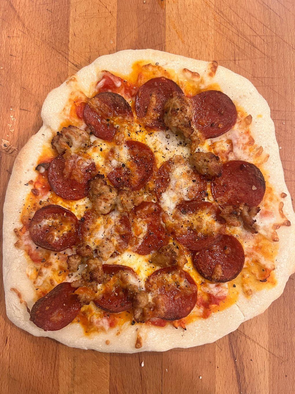 A pizza with pepperoni and sausage on a wooden table.
