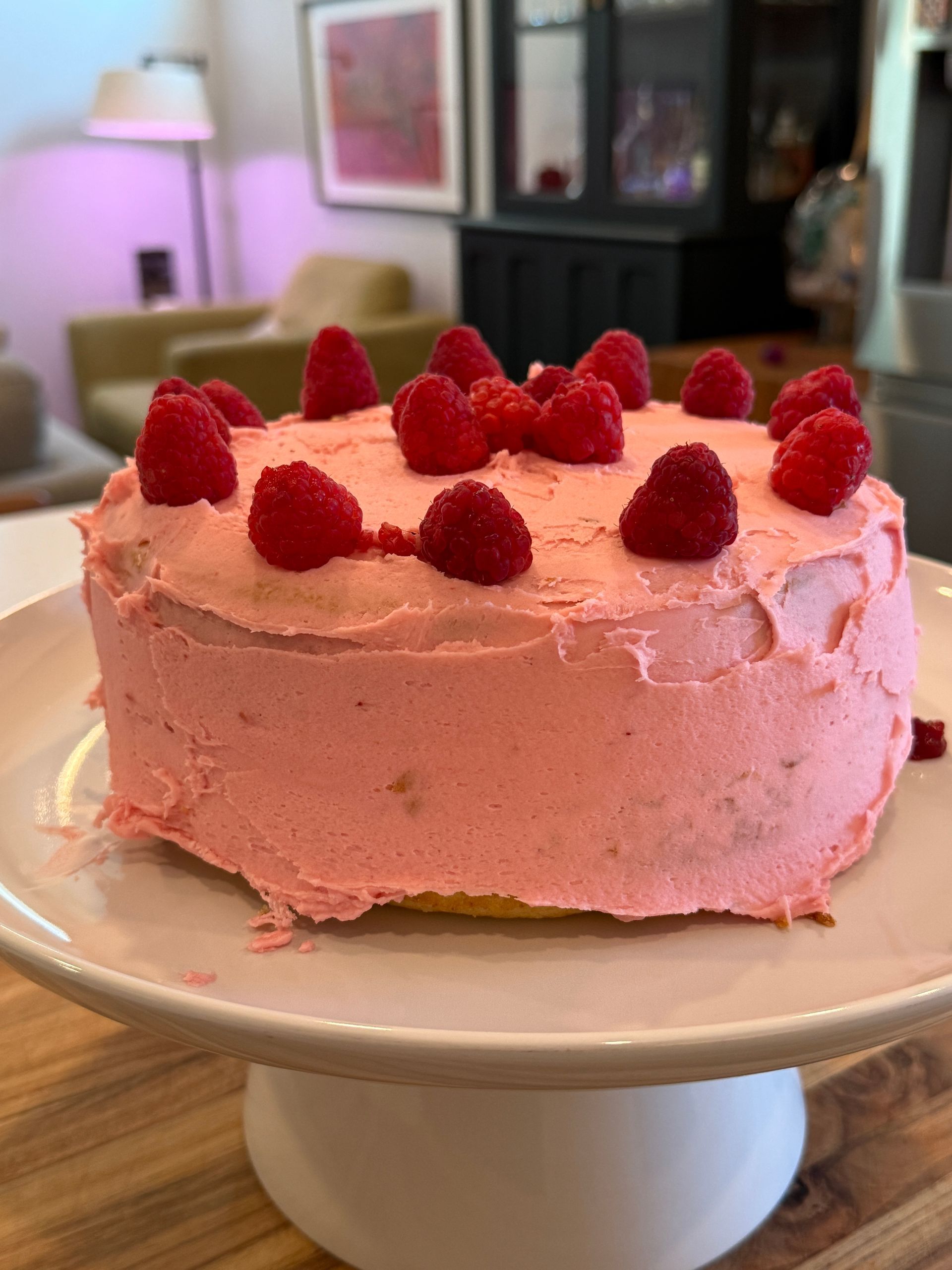 A pink cake with raspberries on top is on a white plate.