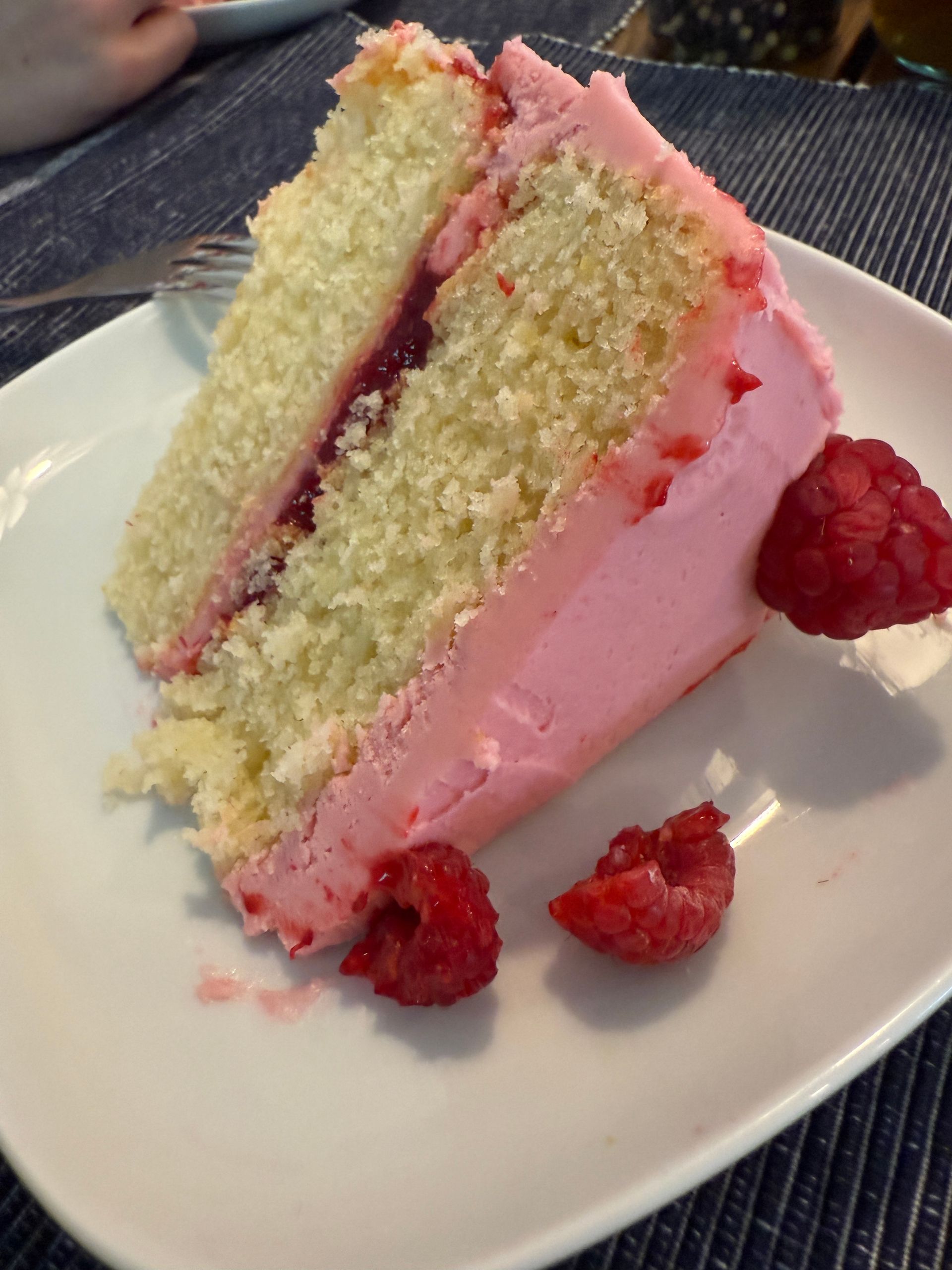 A slice of cake with pink frosting and raspberries on a white plate