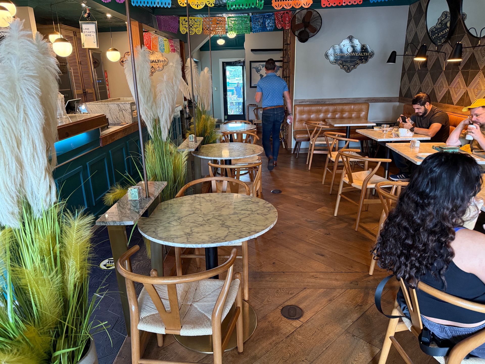 a man walks out of a coffee shop with patrons sitting at tables off to the side