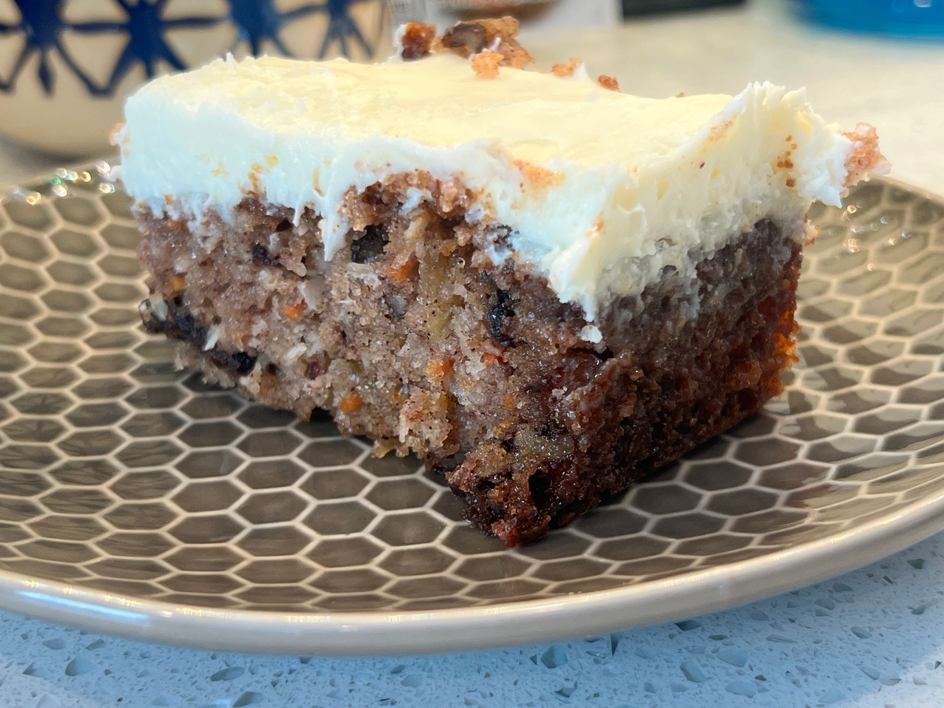A slice of carrot cake with white frosting on a plate.