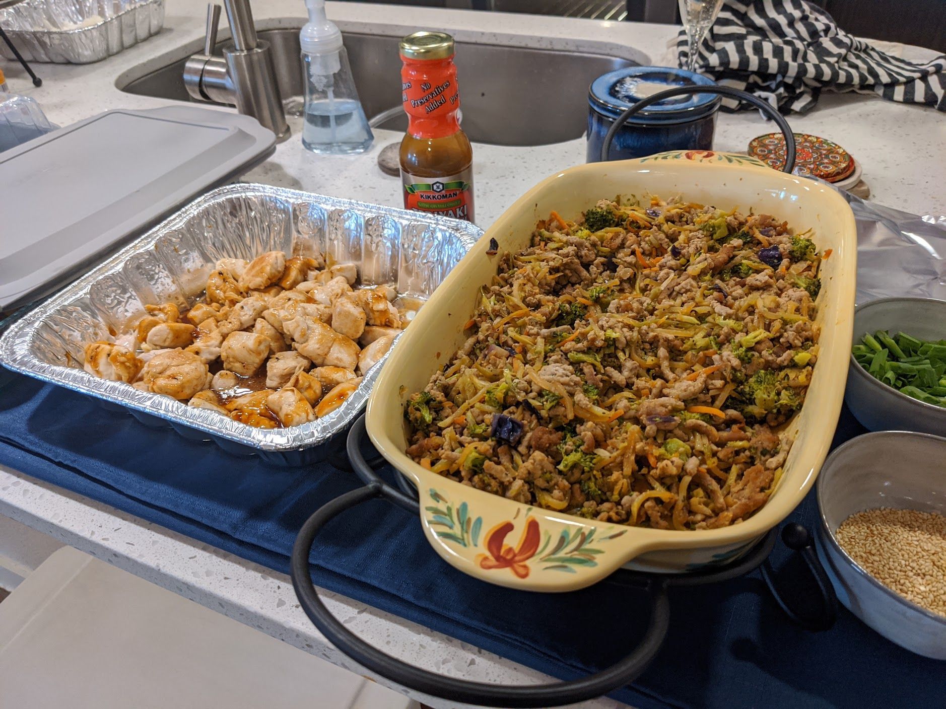 A casserole dish filled with food is sitting on a counter next to a tray of food.