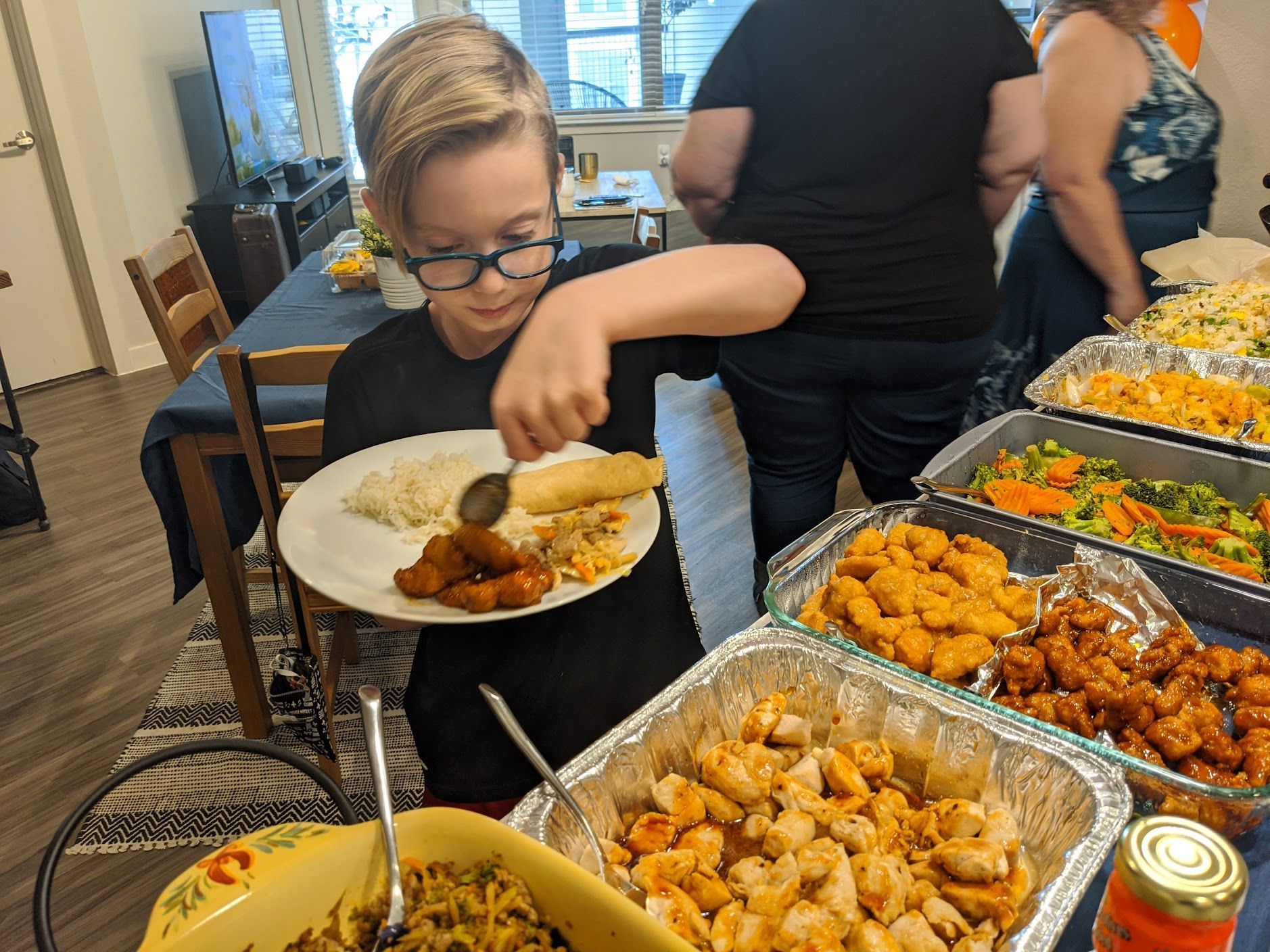 A young boy is eating a plate of food from a buffet table.