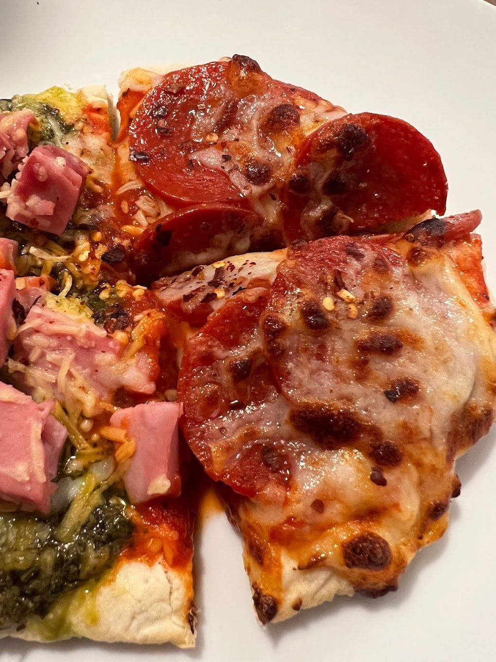 A pizza with pepperoni and ham is on a white plate