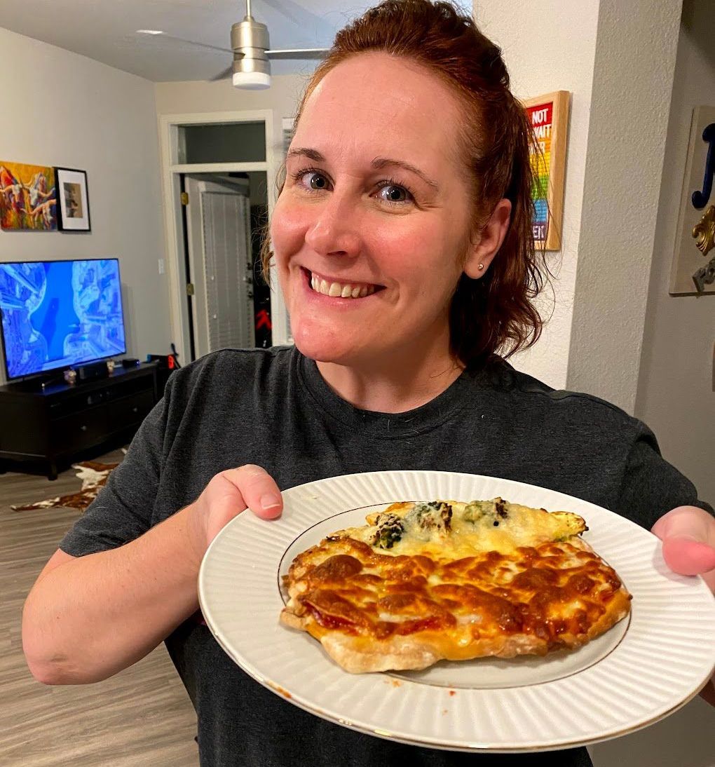 A woman is holding a plate of pizza and smiling.