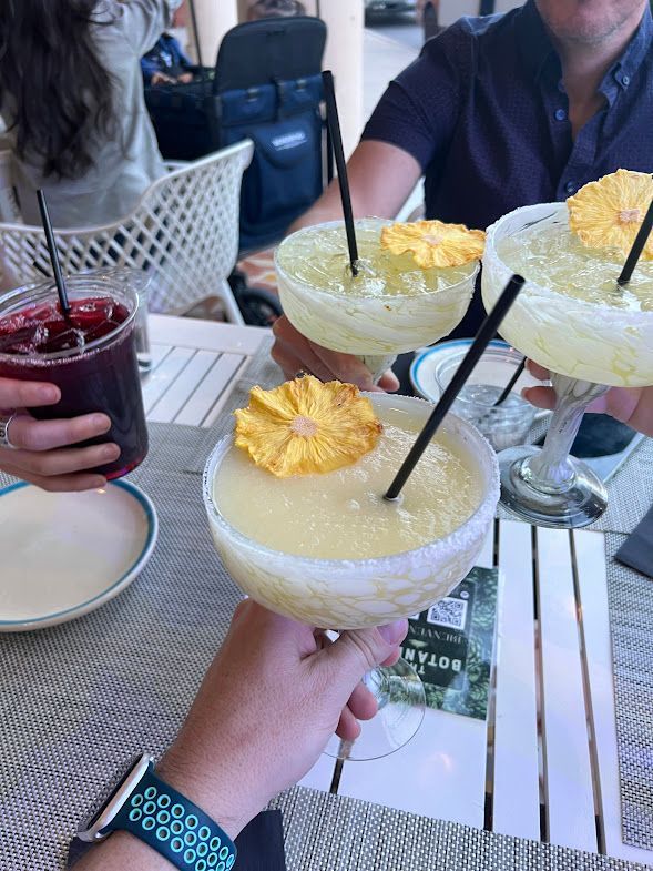 A person is holding a margarita with a pineapple slice on top.