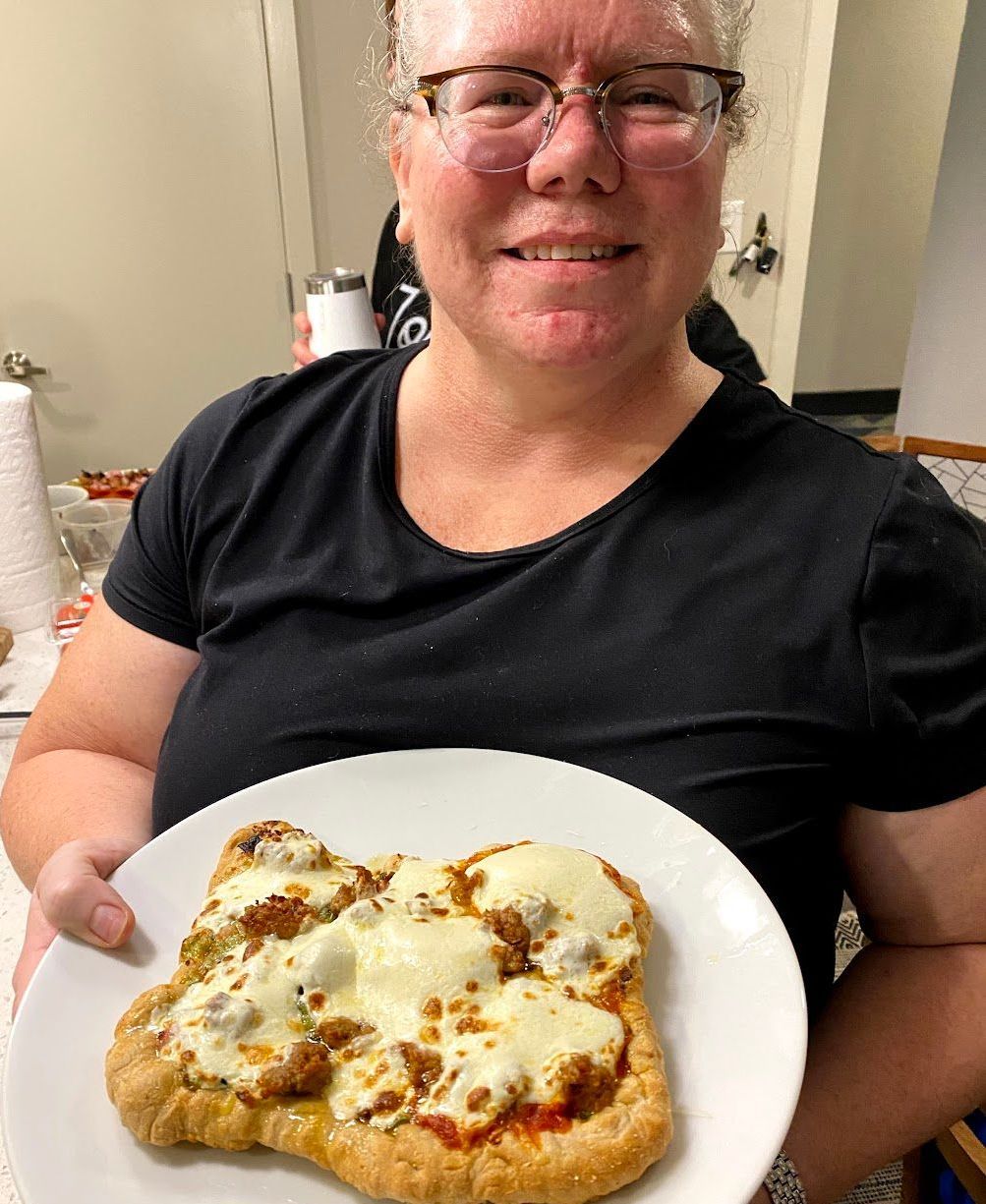 A woman is holding a white plate with a pizza on it.