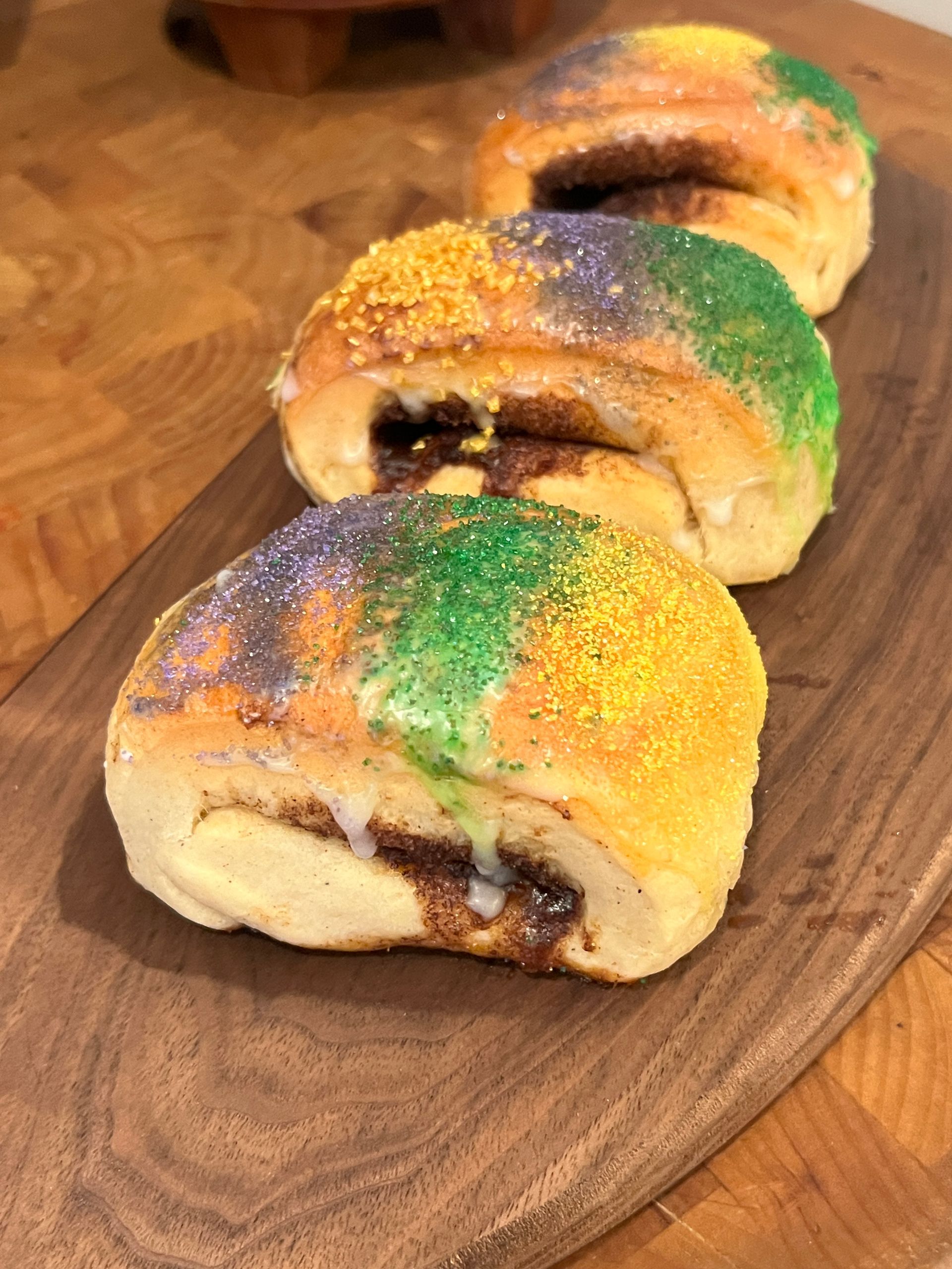 Three king cakes are sitting on a wooden cutting board.