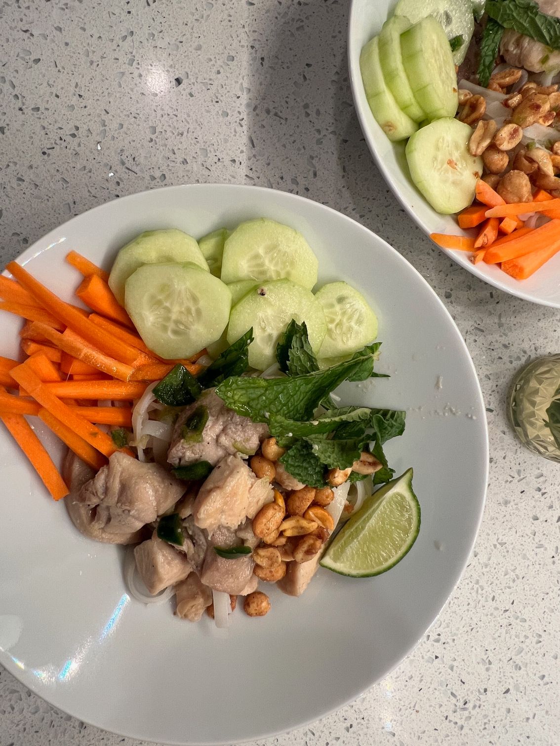 A white plate topped with chicken , carrots , cucumbers and peanuts.