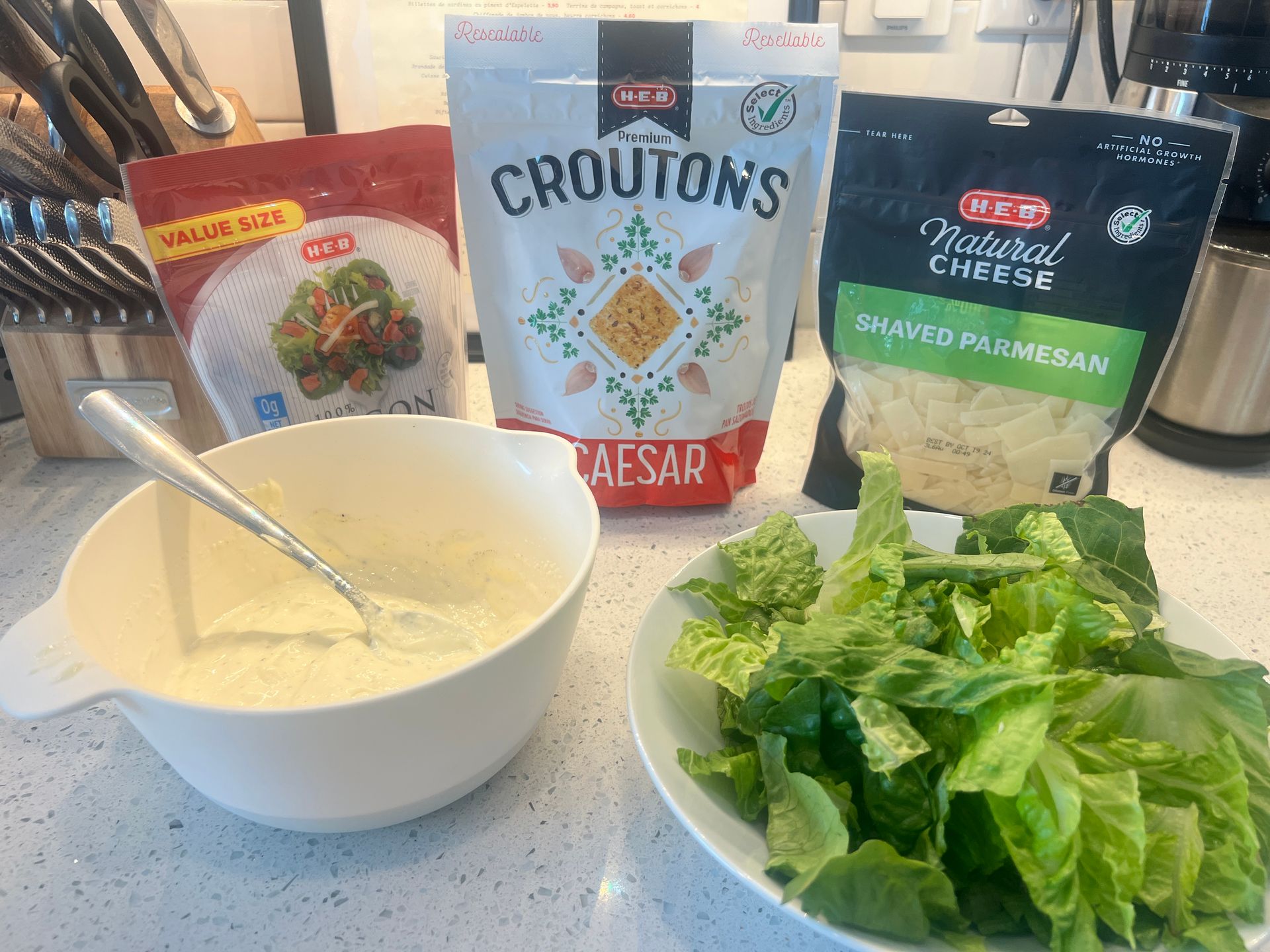 There is a bowl of dressing next to a bowl of lettuce.