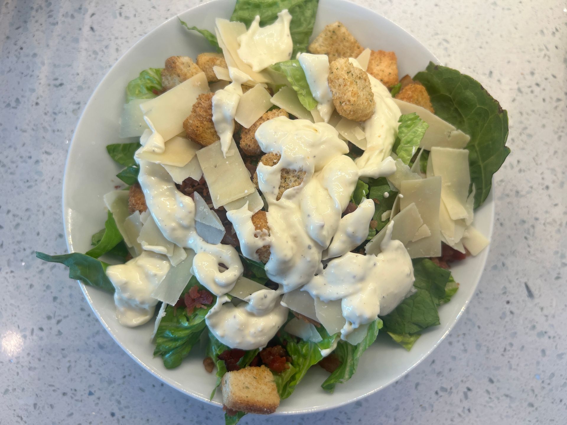 A salad with lettuce , croutons , cheese and dressing on a white plate.