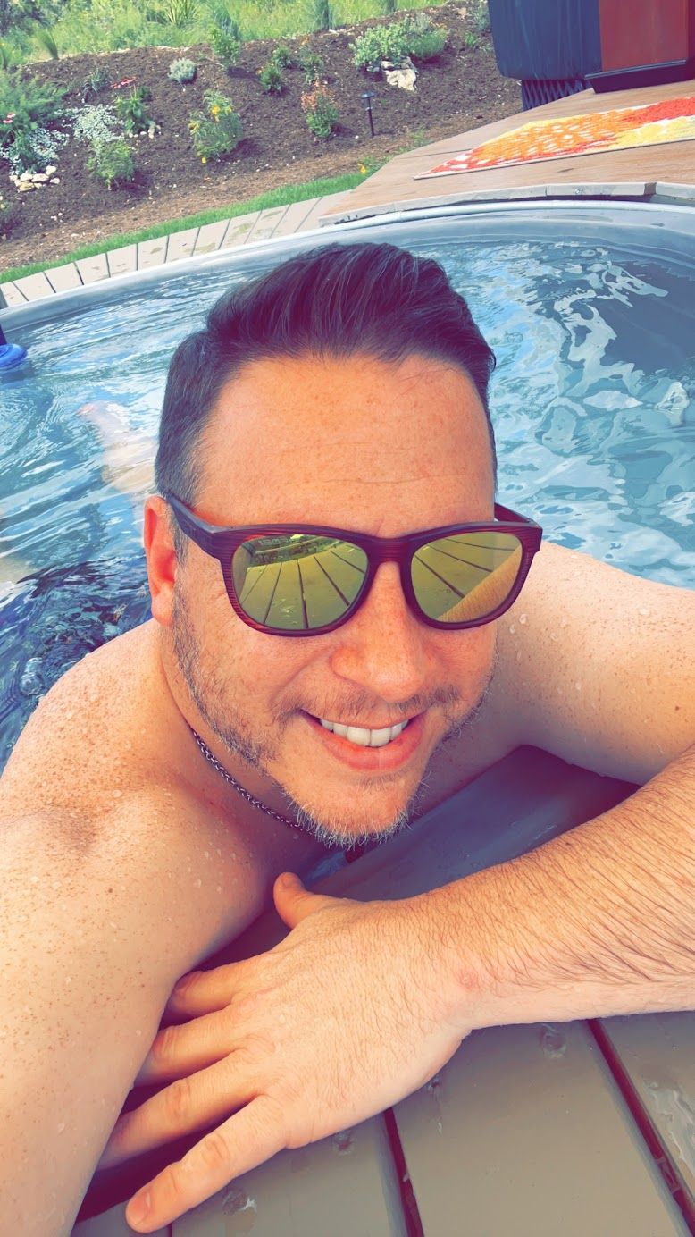 A man wearing sunglasses is laying in a hot tub.