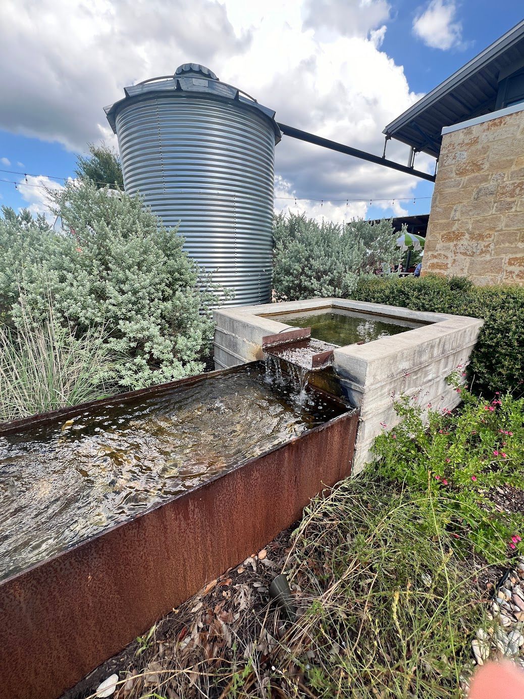 A water fountain with a silo in the background and a building in the background.