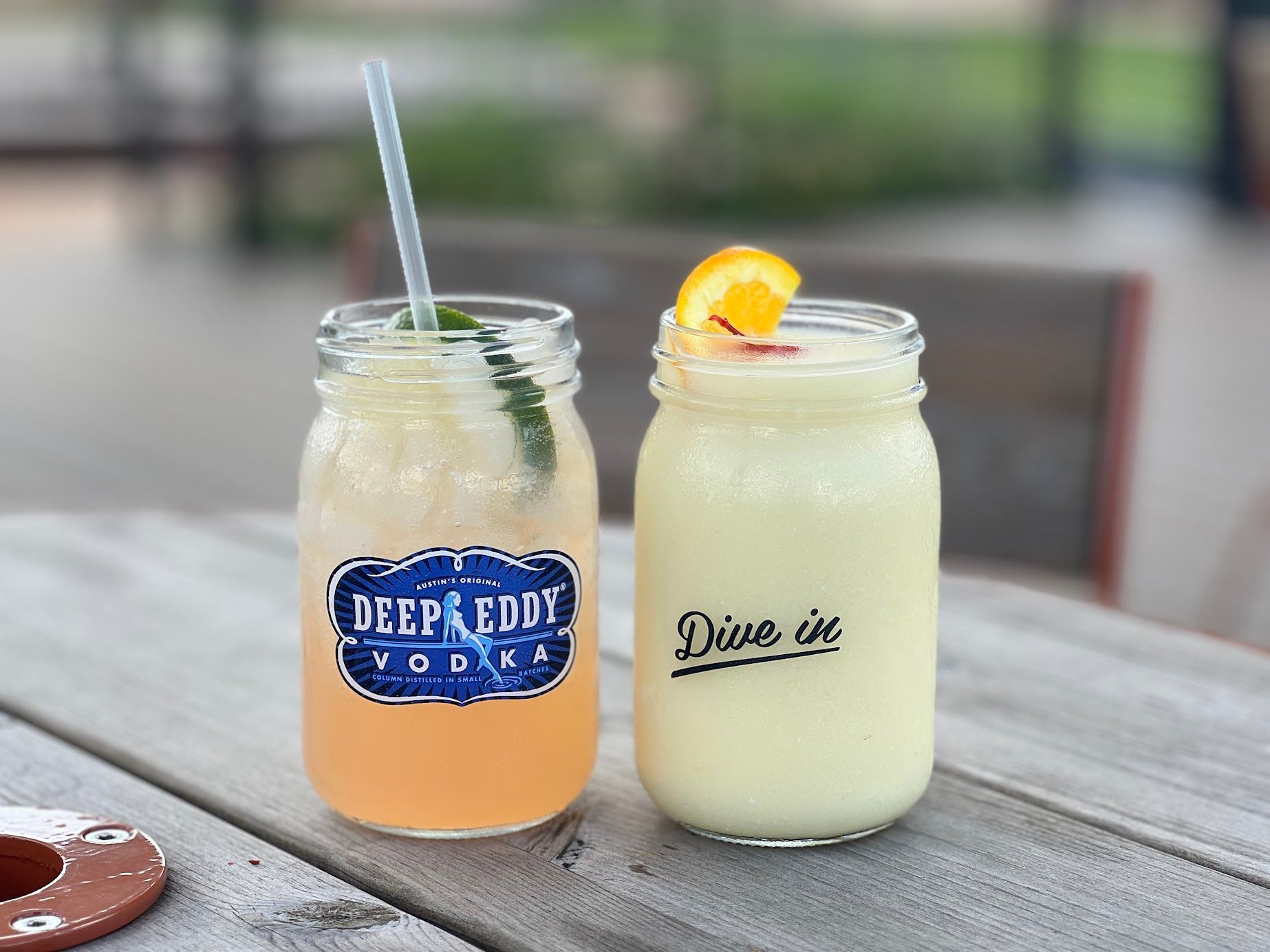 Two mason jars filled with different types of drinks are sitting on a wooden table.