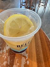 A cup of lemonade with ice and a slice of lemon on a wooden table.