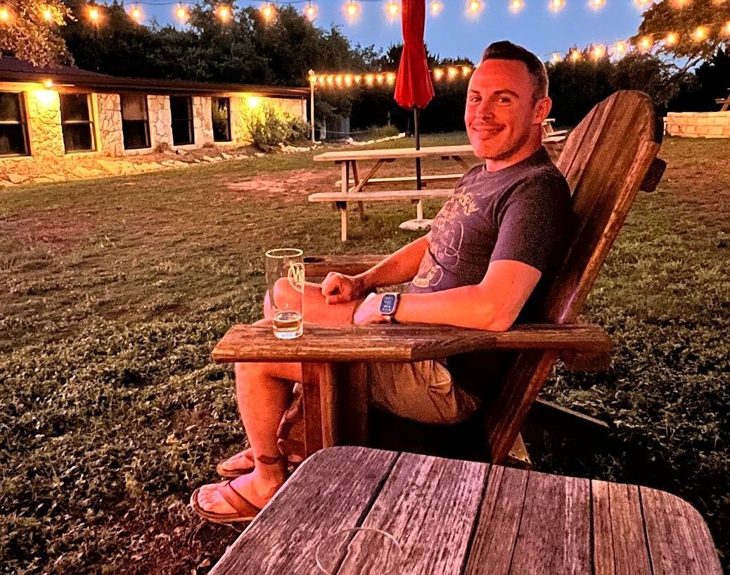 A man is sitting in a wooden chair holding a glass of wine.