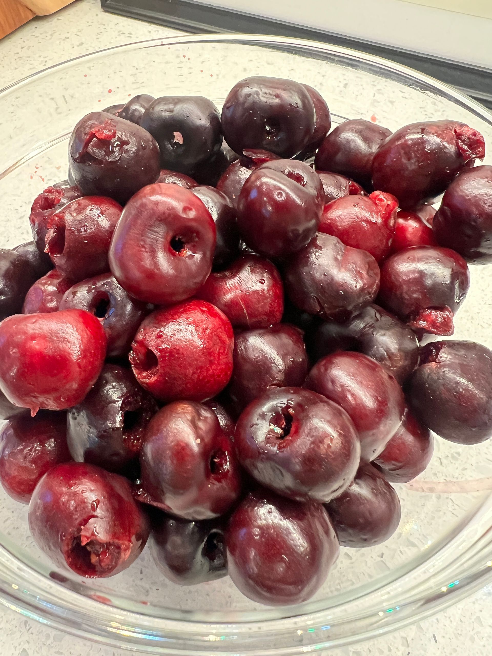 A glass bowl filled with cherries is sitting on a counter.