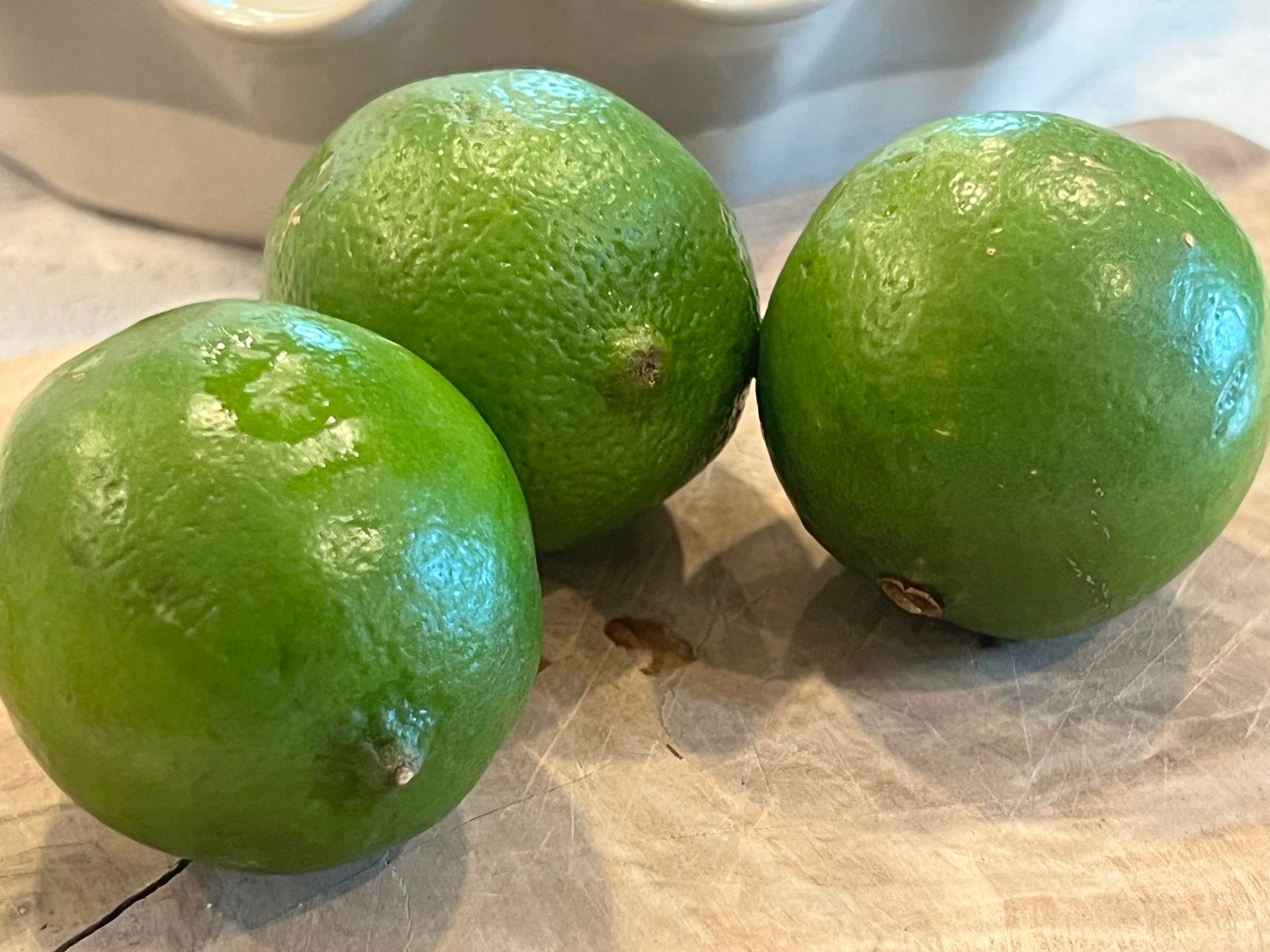 Three limes are sitting on a wooden cutting board.