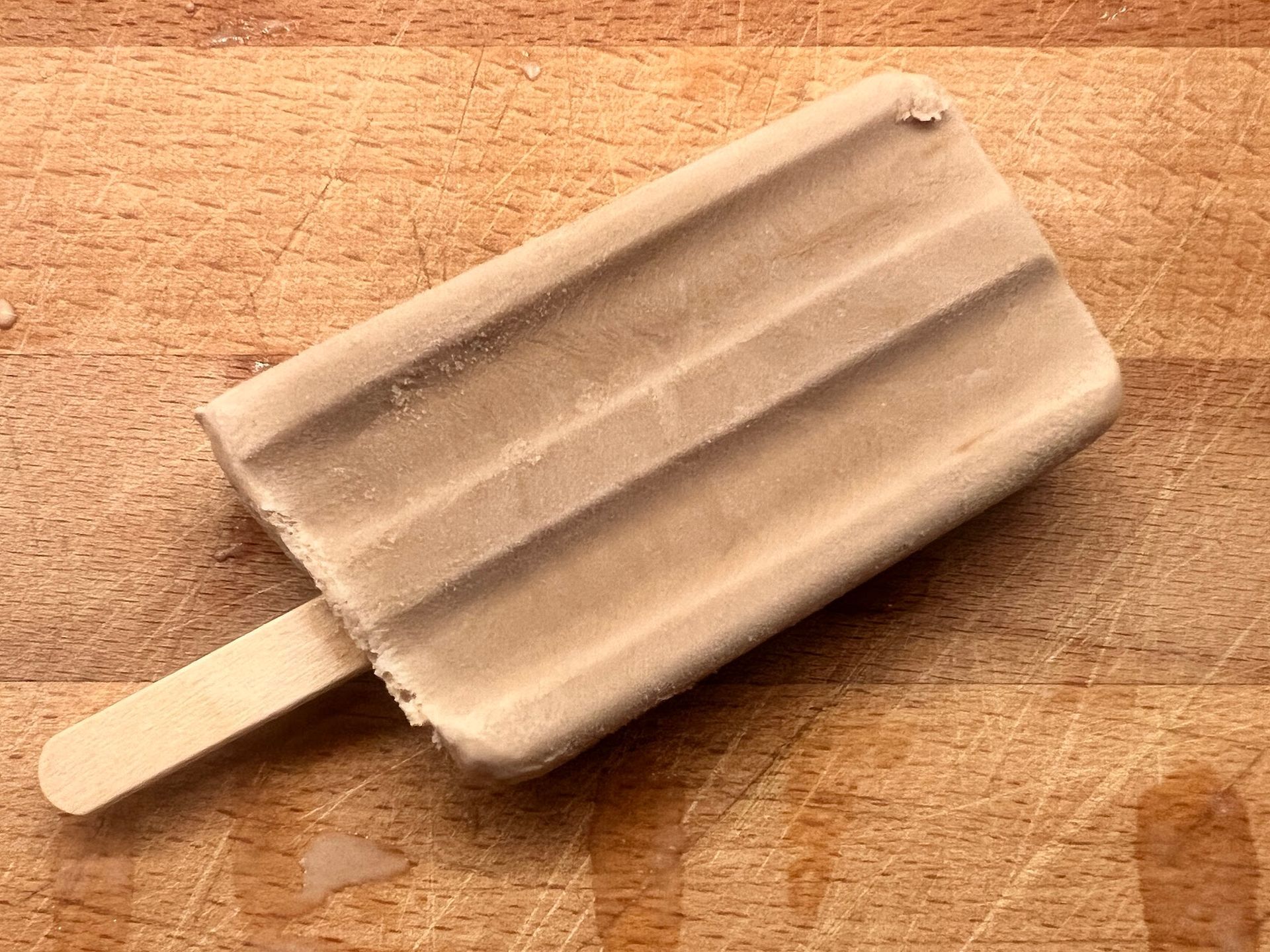 A popsicle is sitting on a wooden cutting board.