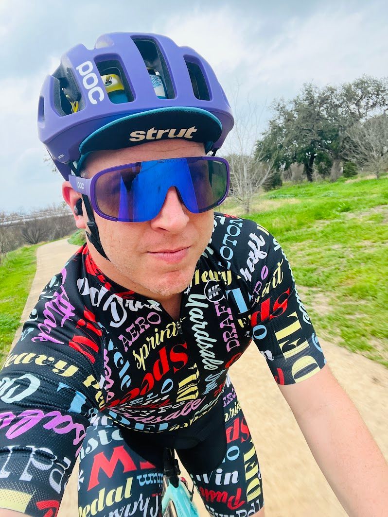 A man wearing a purple helmet and sunglasses is riding a bike on a dirt road.