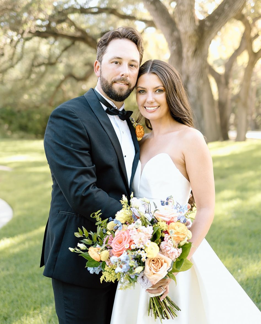 A bride and groom are posing for a picture while the bride is holding a bouquet of flowers.