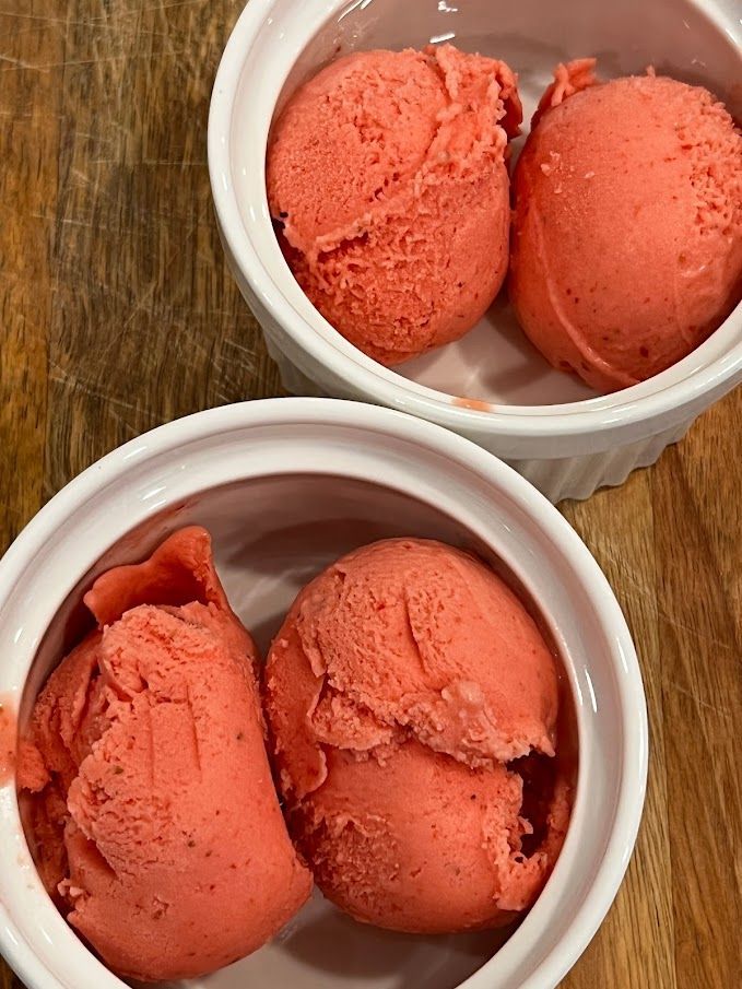Two bowls of strawberry ice cream on a wooden table