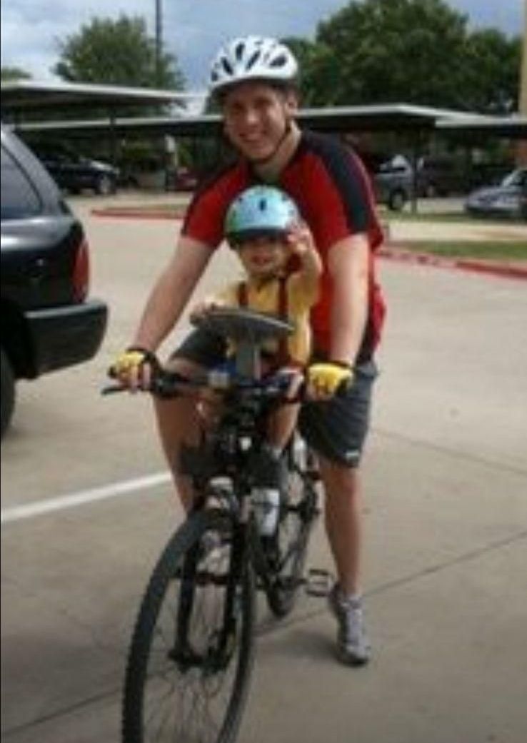 A man is riding a bike with a child on the back seat