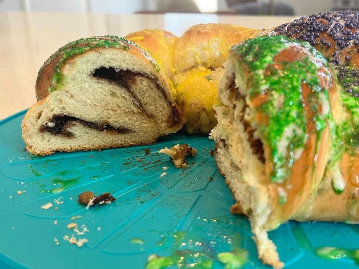 A king cake with a slice taken out of it is on a blue plate.