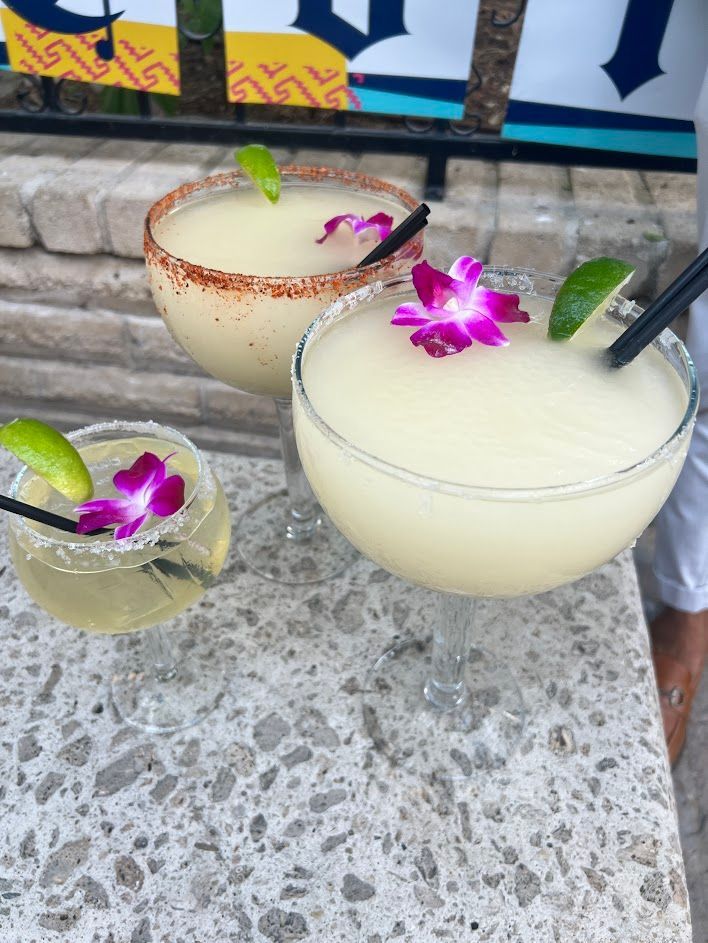 Three margaritas with straws and flowers on a table.