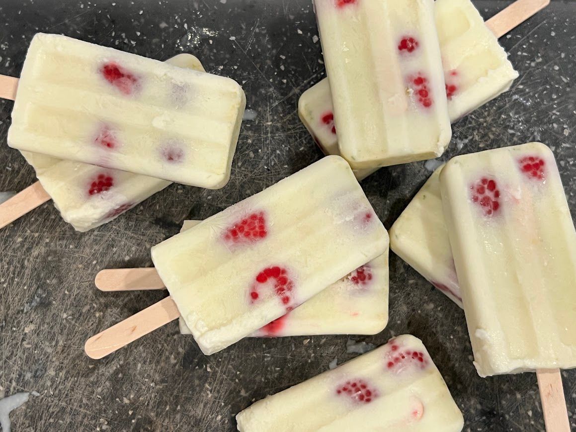 A bunch of white popsicles with raspberries on them
