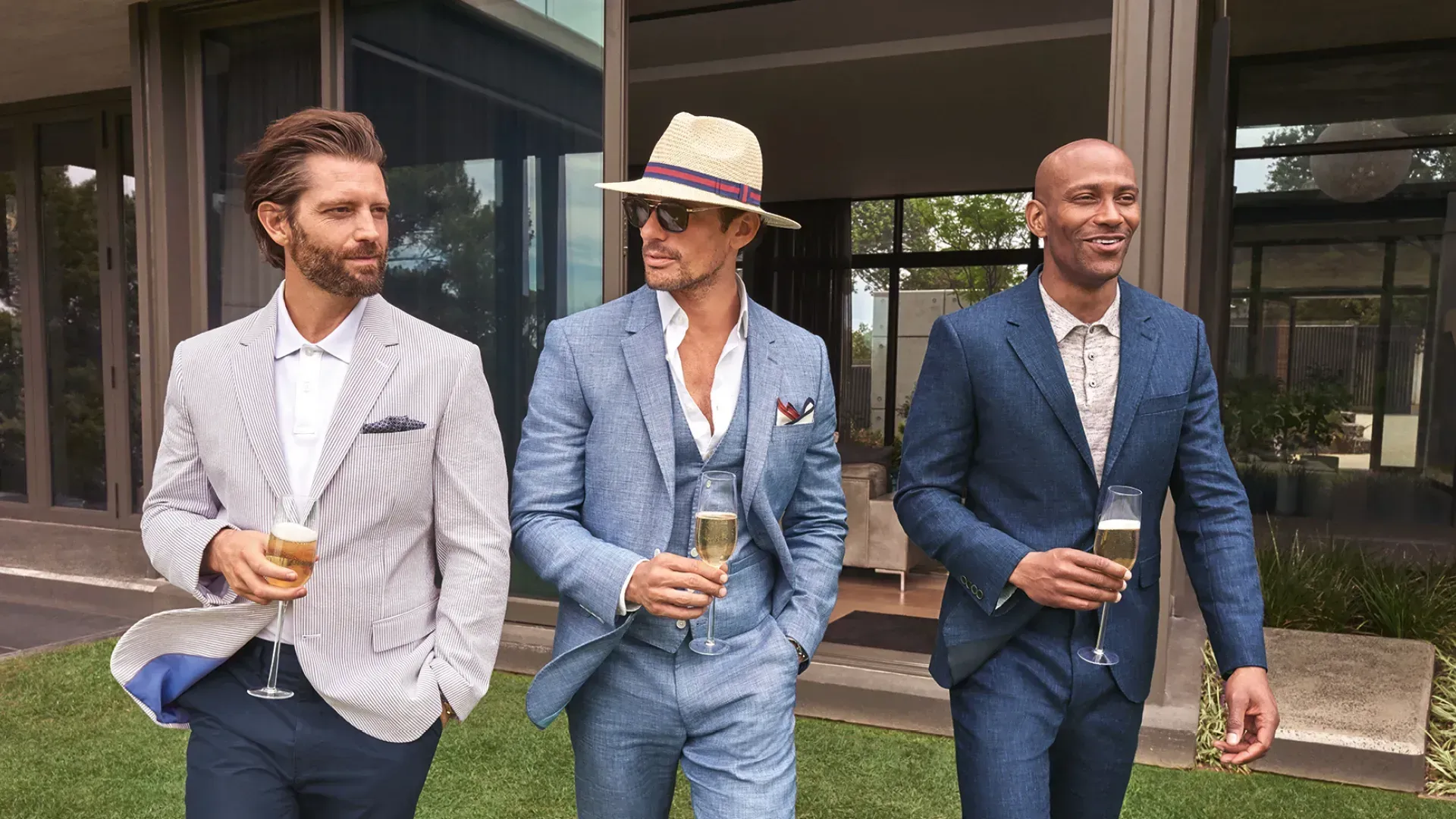 Three men in suits and hats are standing next to each other holding champagne glasses.