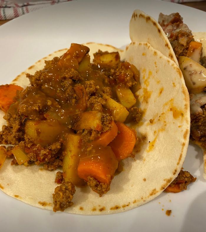 A close up of a taco with meat and vegetables on a plate.