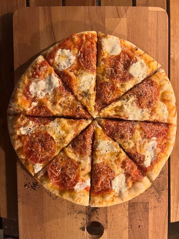A pizza is cut into slices on a wooden cutting board.