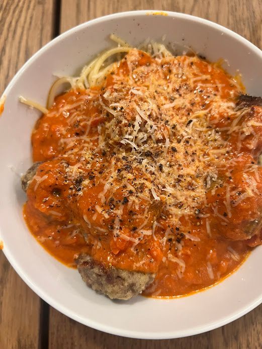 A bowl of spaghetti and meatballs with sauce and cheese on a wooden table.