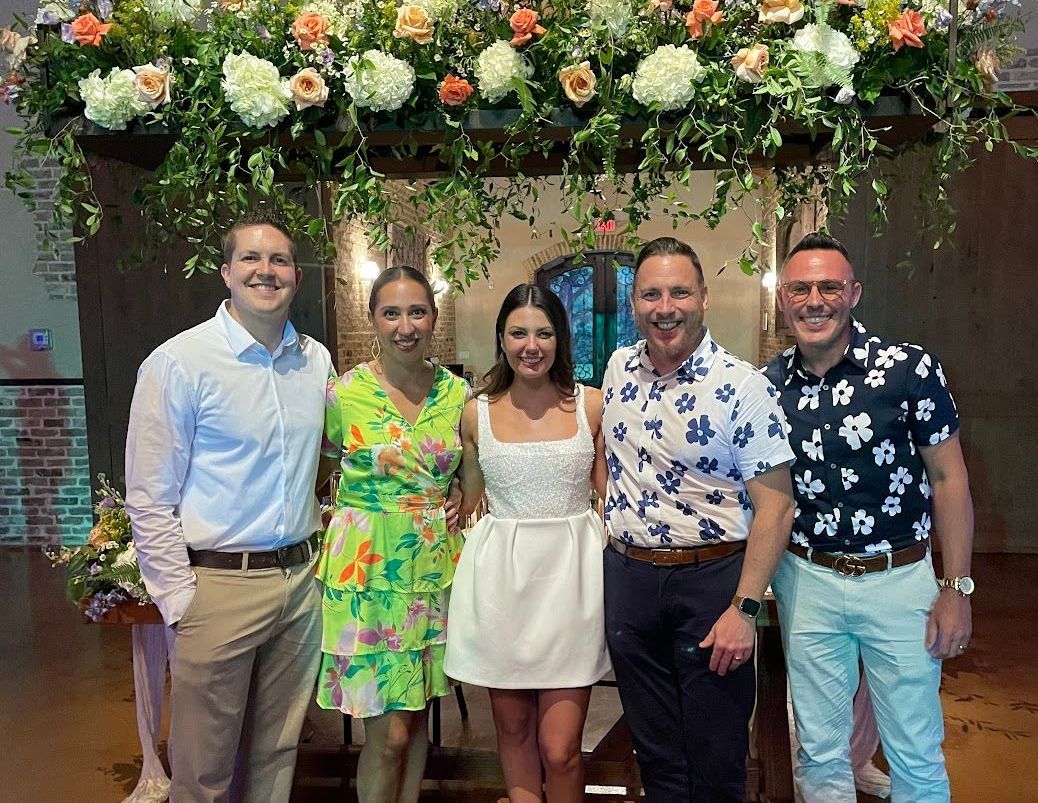 A group of people are posing for a picture in front of a floral arch.