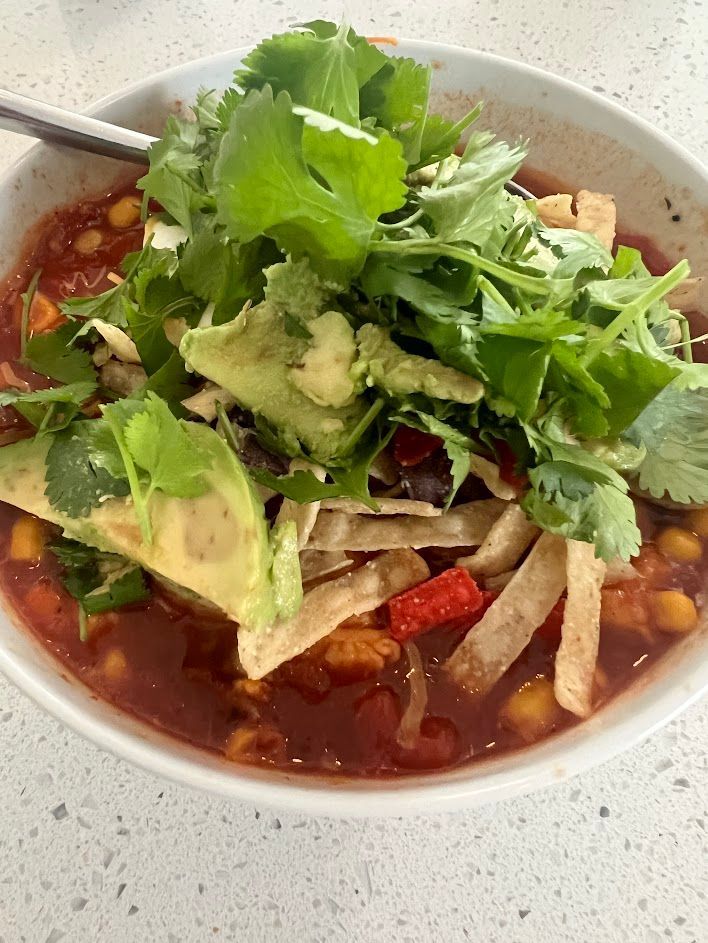 A bowl of soup with avocado and cilantro on top