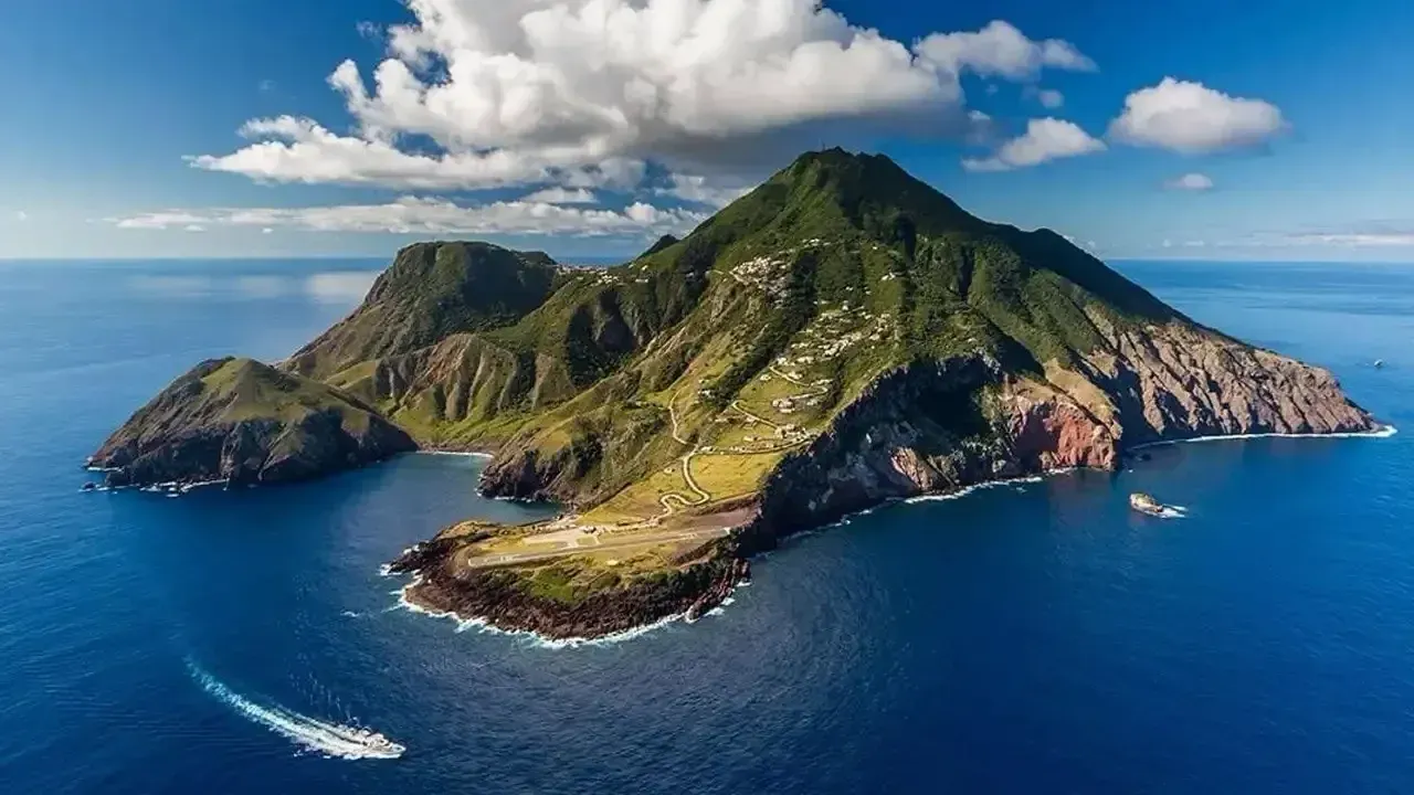 A lush green island rising from bright blue ocean under a partly cloudy sky