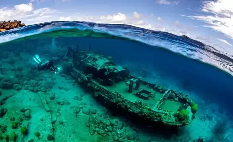 Sunken shipwreck beneath clear turquoise ocean water near a reef and surface waves