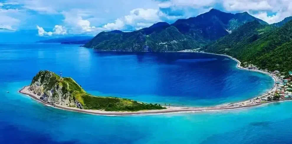 Aerial view of a turquoise tropical bay with a curved white-sand beach and lush green mountains